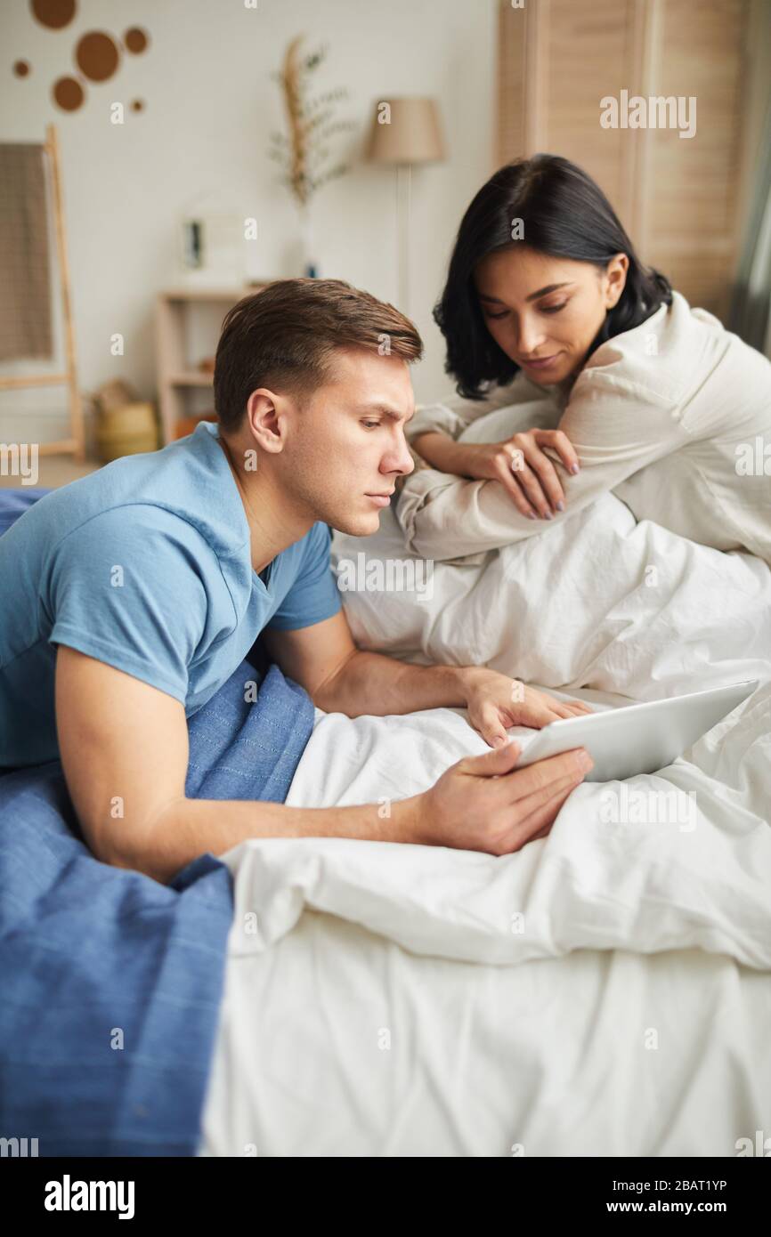 Ritratto ad alto angolo di una giovane coppia moderna utilizzando un tablet digitale mentre si siede a letto a casa e ordinare cibo online o guardare film Foto Stock