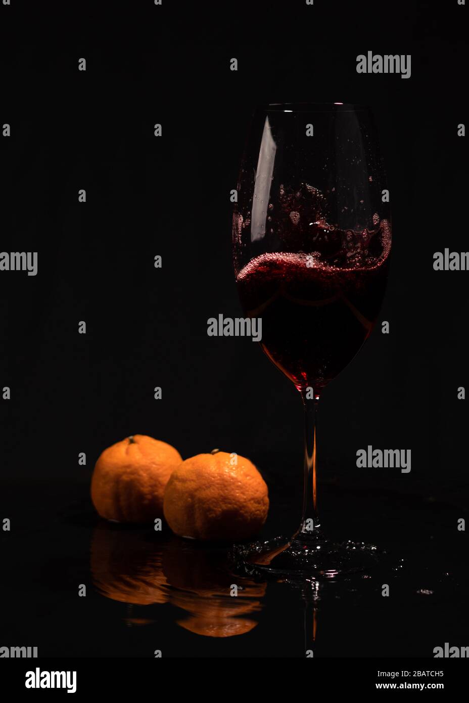 Ancora vita con il bicchiere di vino nero. Vino rosso su sfondo nero. Mandarini con vino rosso su sfondo nero. Foto Stock