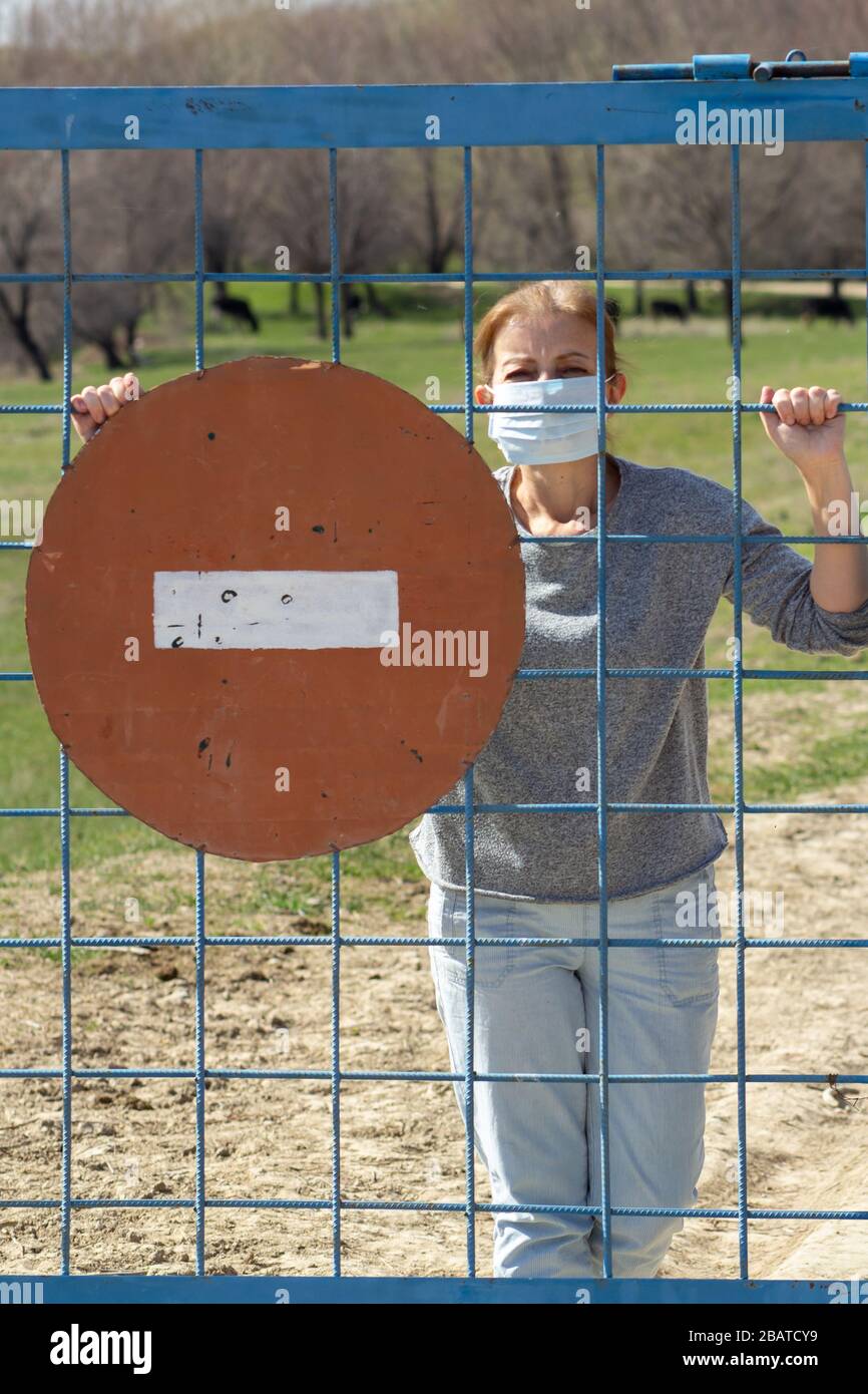 Le donne caucasiche sono in maschera protettiva dietro cancello chiuso con segno di stop rosso in quarantena per coronavirus covid-19 . Concetto di soggiorno a casa Foto Stock