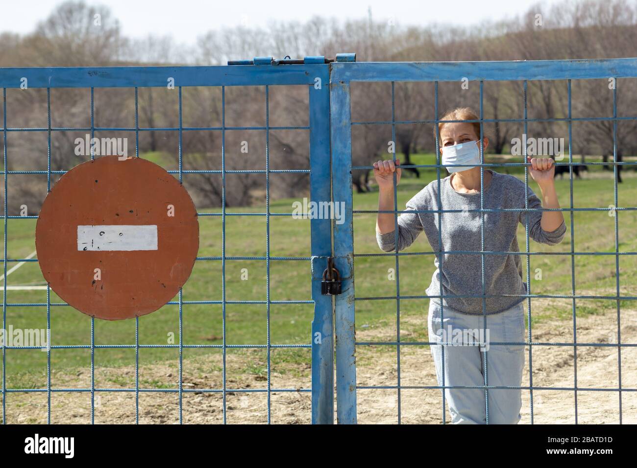 Le donne caucasiche sono in maschera protettiva dietro cancello chiuso con segno di stop rosso in quarantena per coronavirus covid-19 . Concetto di soggiorno a casa Foto Stock