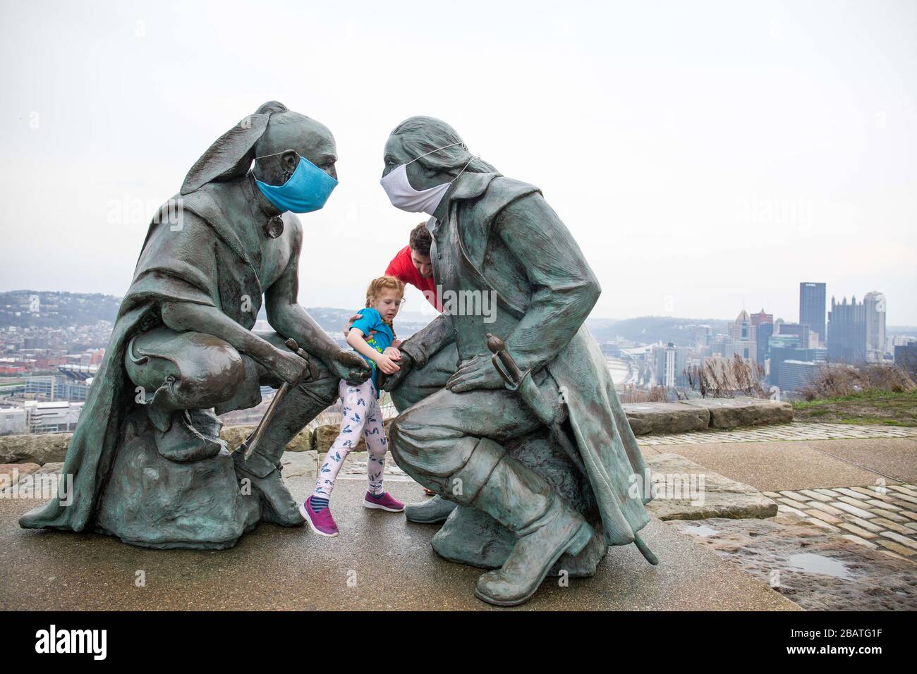 Pittsburgh, Pennsylvania, Stati Uniti. 28 Marzo 2020. NOVITÀ in risposta al virus COVID-19 una persona intelligente ha messo le maschere sul leader della Seneca Guyasuta, a sinistra e George Washington. La statua è chiamata "punti di vista". Si affaccia sulla città di Pittsburgh, Pennsylvania. La città è stata in un ordine di "soggiorno a casa" dal governatore Wolf dal 23 marzo 2020. La statua segna l'estremità più occidentale di He Grand View Scenic Byway, una Pennsylvania Scenic Byway ufficiale. Un padre e una figlia prendono un rapido tour del parco dopo aver lasciato il cibo fuori ad un parente. Credit: Annie o'Neill/ZUMA Wire/Alamy Live News Foto Stock