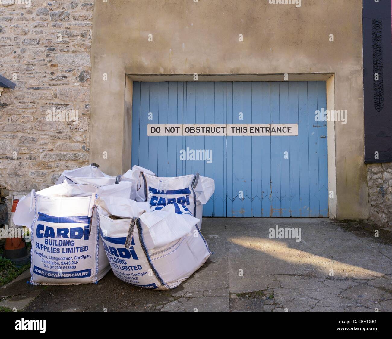 Entrata con cartello che dice 'non ostruire questa entrata' con borse mercantili costruttori che ostruiscono l'entrata. Newport, Pembrokeshire. Galles. REGNO UNITO Foto Stock