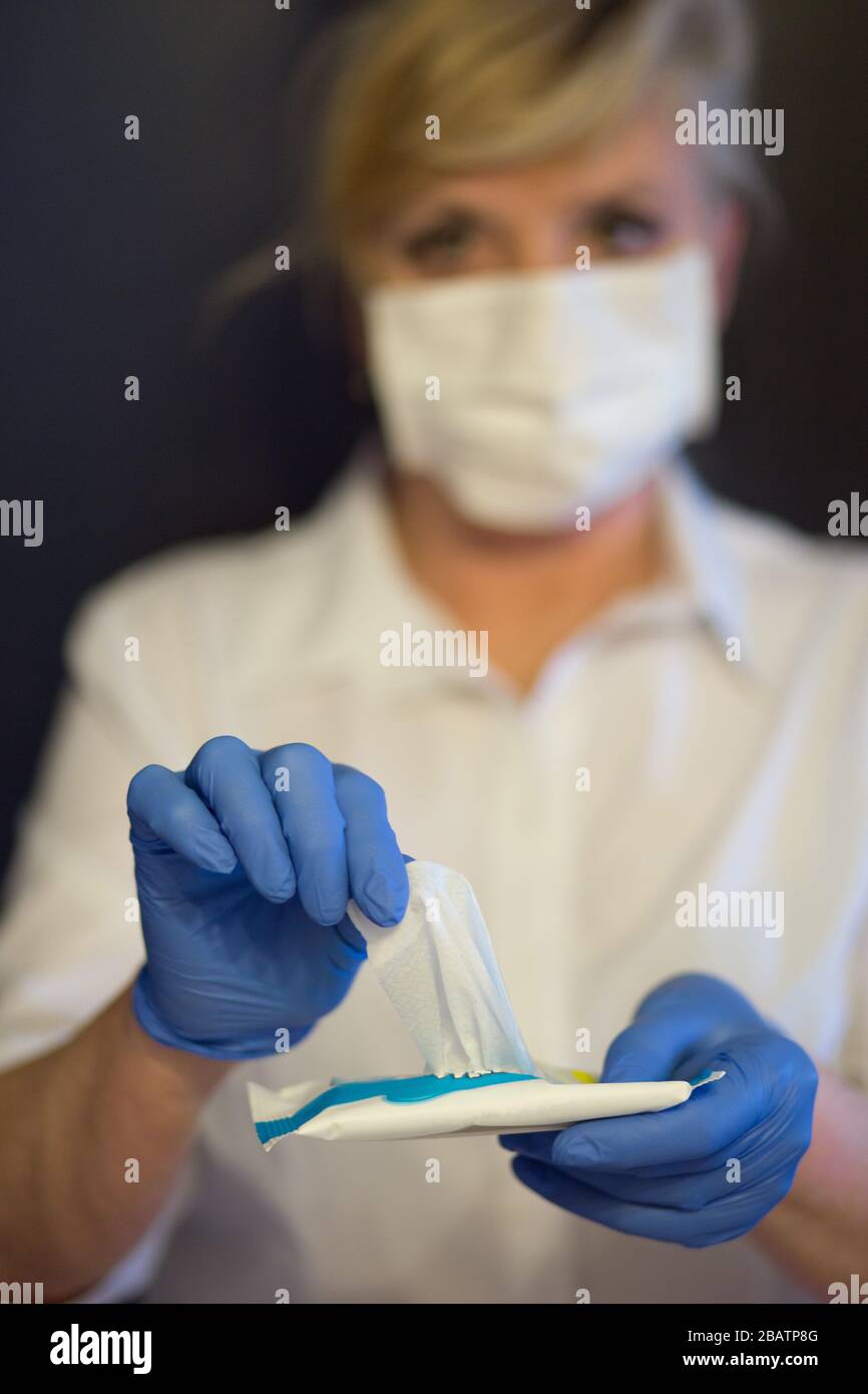 Donna anziana che indossa la maschera, guanti prende un panno umido. Messa a fuoco selettiva. Coronavirus e sintomi di virus epidemici. Foto Stock