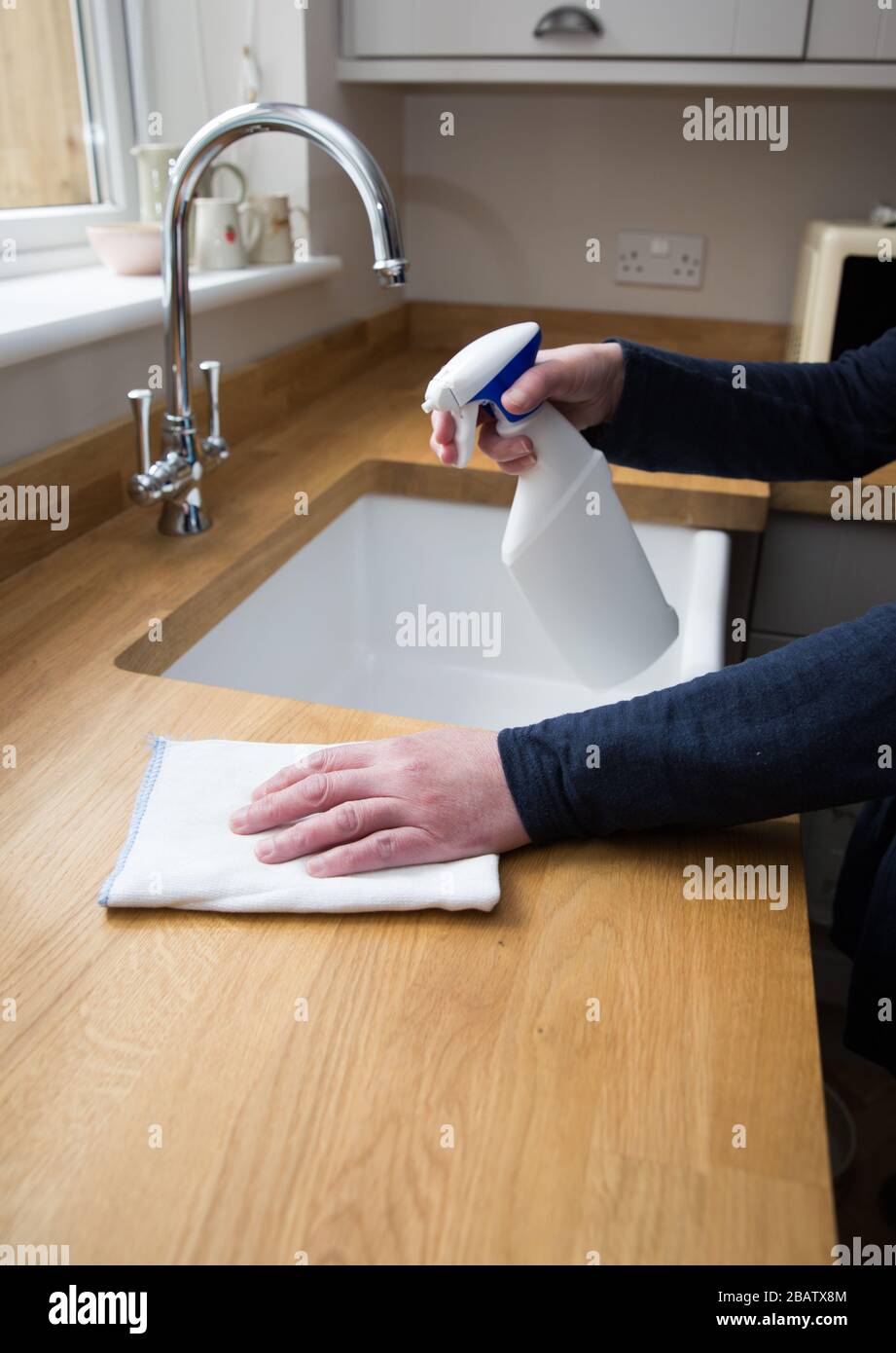 Un primo piano di un paio di mani umane che puliscono l'interno di una cucina con spray antibatterico per disinfettare le superfici di lavoro durante Coronavirus Foto Stock