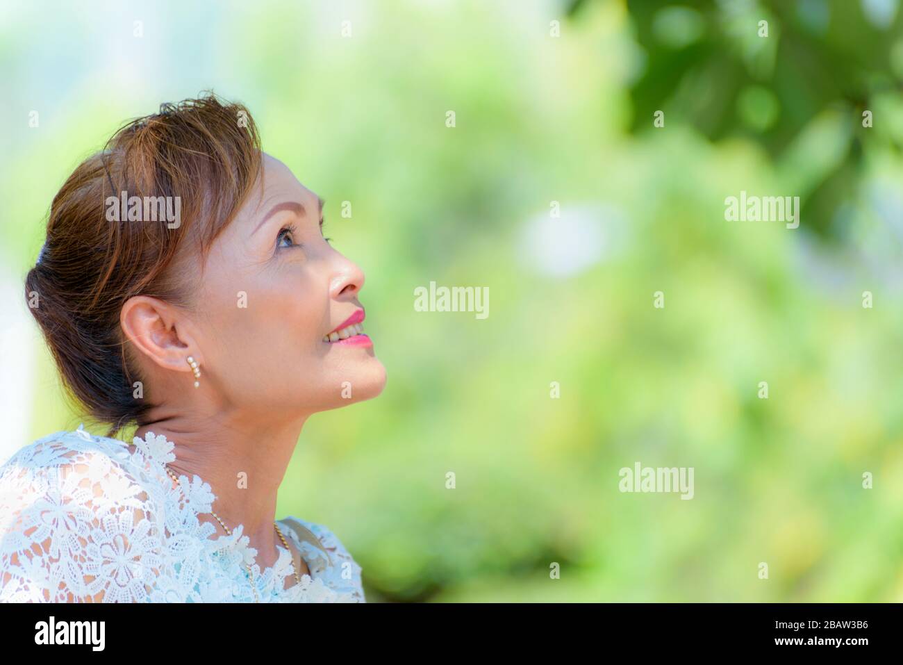 Faccia laterale di closeup di un sano vestito asiatico di mezza età donna in stile tailandese vestiti, ritratto vecchia signora riposante all'aperto guardando su sorridente felice nel Foto Stock