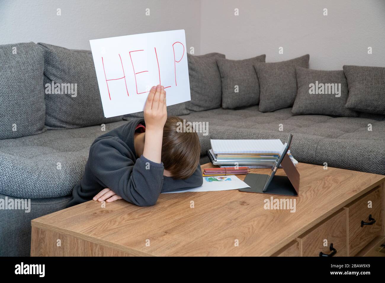 Difficoltà di apprendimento. Triste stanco ragazzo frustrato seduto al tavolo con molti libri e tenendo carta con parola Aiuto. Concetto di istruzione. Foto Stock