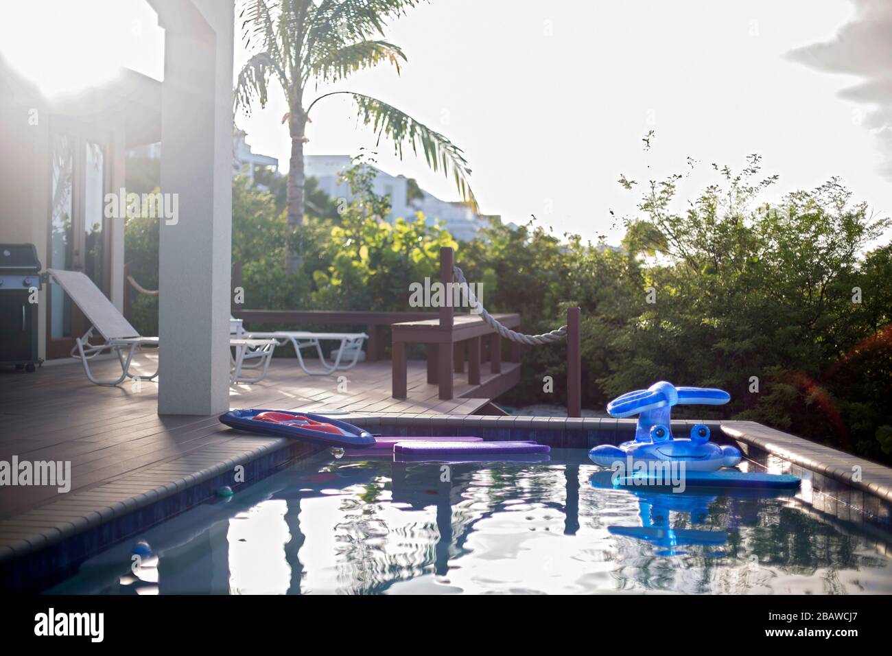 Piscina nella casa tropicale per vacanze con galleggianti e mobili da patio al tramonto. Foto Stock