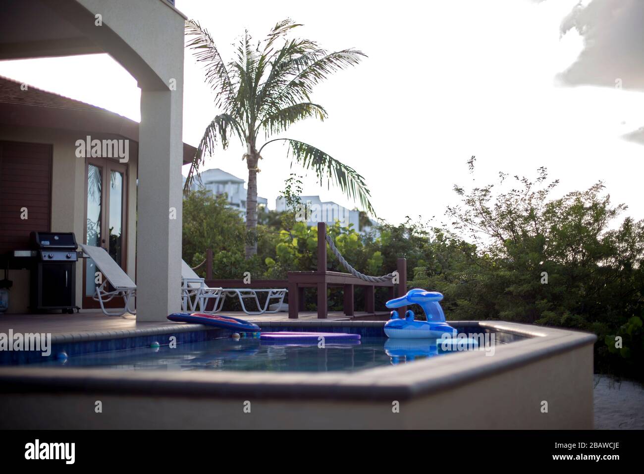 Piscina nella casa tropicale per vacanze con galleggianti e mobili da patio al tramonto. Foto Stock