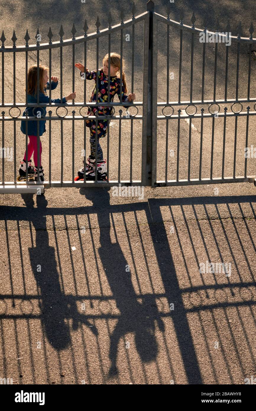 Due ragazze piccole con rulli della lama che chiacchierano e che giocano alla recinzione del cortile che getta le ombre lunghe al tramonto Foto Stock