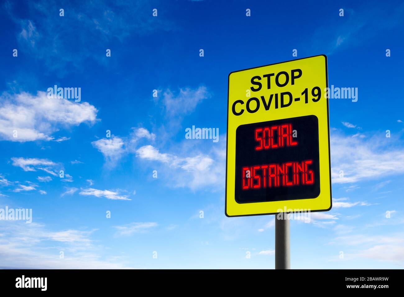 Un segno Stop COVID-19 con un messaggio digitale luminoso sulle distanzazioni sociali e con spazio di copia contro il cielo blu. Concetto di prevenzione della diffusione del c Foto Stock