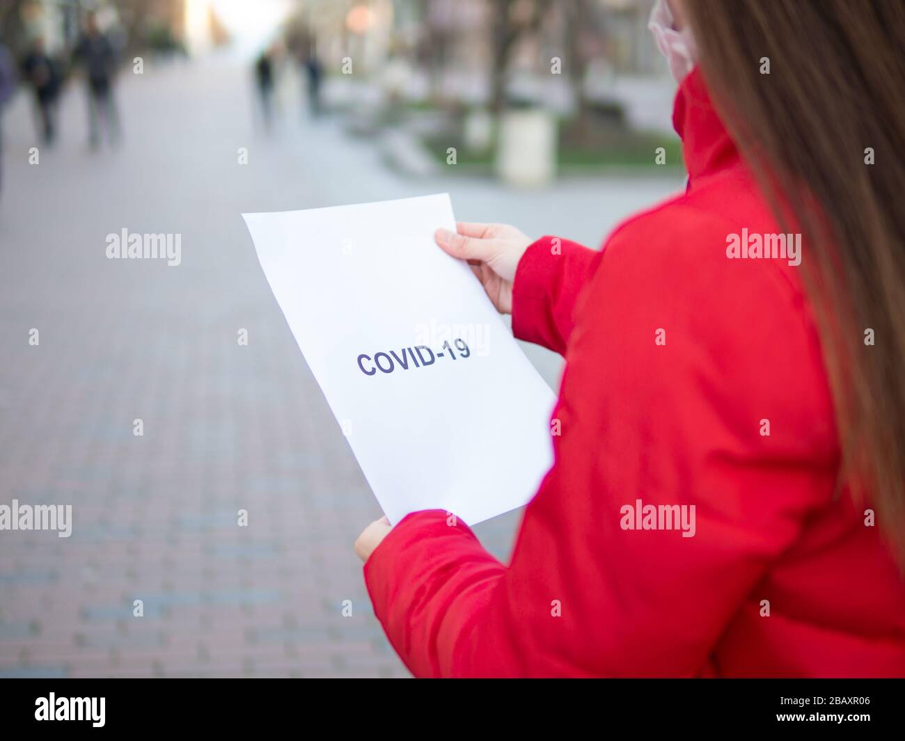 Una donna in piedi all'aperto che tiene un stampato su carta bianca con covid-19 testo stampato su di esso. Concetto di pubblicità pandemica di coronavirus Foto Stock