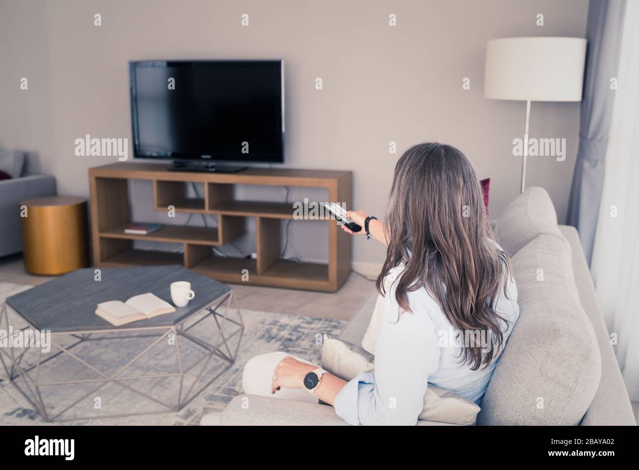Una donna su un divano che si prepara a guardare la TV Foto Stock