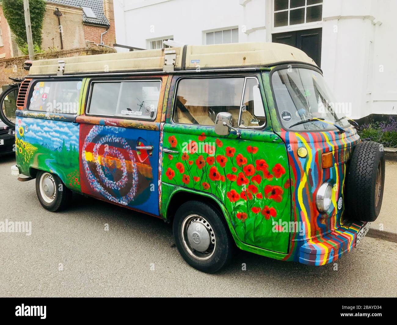 Camper VW con decorazione "hippie" – arte di strada mobile su una Volkswagen Kombi. Parcheggiato in strada con una casa bianca sullo sfondo. Foto Stock