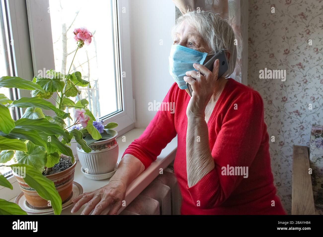 Il Covid-19, salute, sicurezza e pandemia concetto - vecchia donna solitaria anziano seduta vicino alla finestra Foto Stock