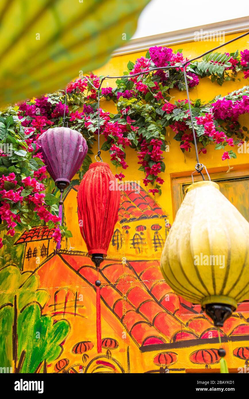 Lanterna di carta colorata appesa alla casa tradizionale di stile vietnamita con arte murale e fiori rosa. Foto Stock