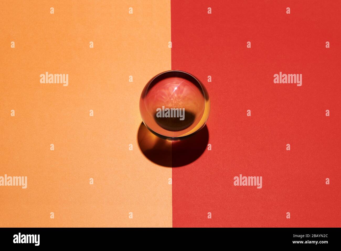 Sfera di vetro su uno sfondo diviso arancione e rosso posto al centro sulla linea di divisione con una miscela interna di colore Foto Stock