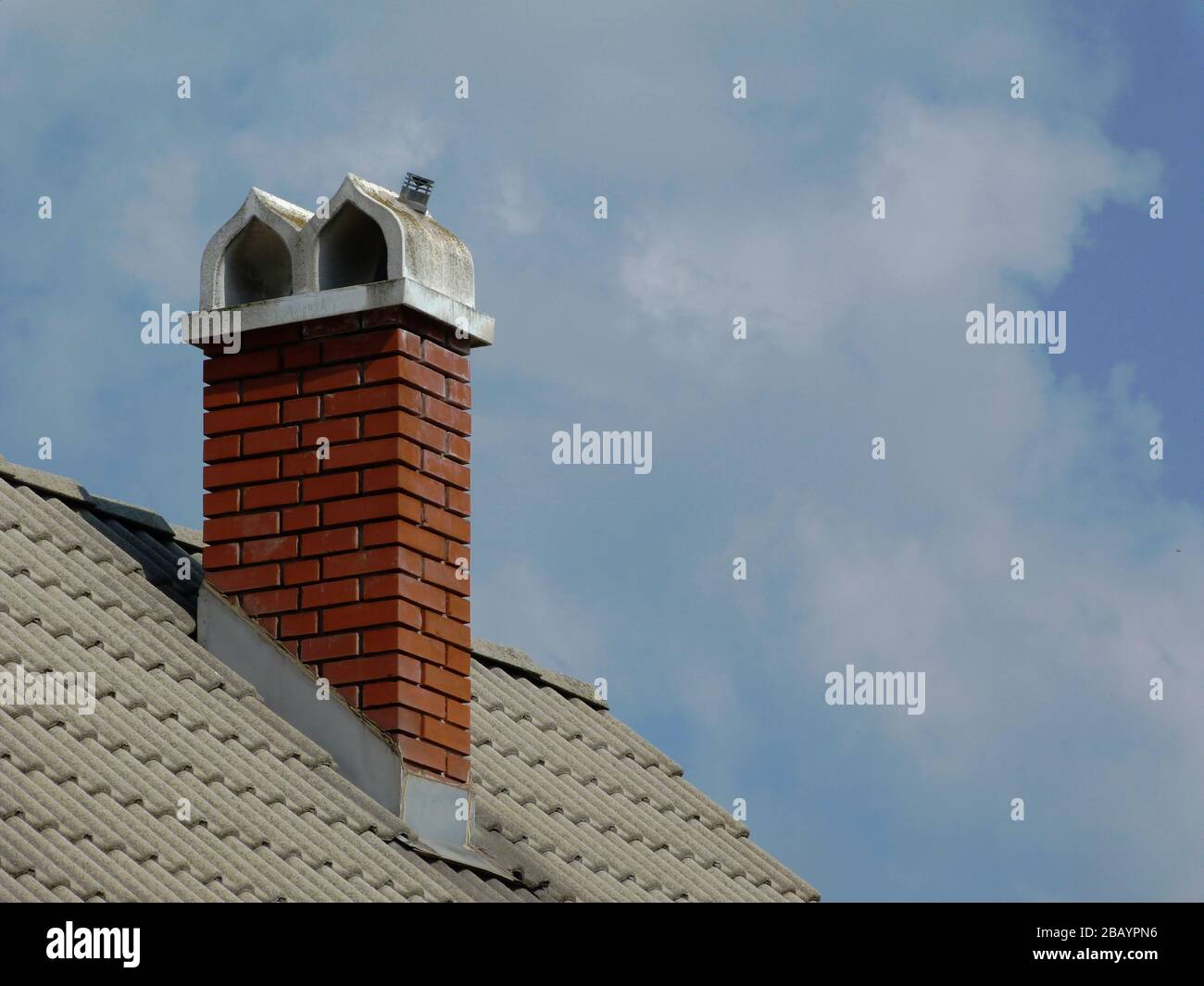 stile retrò camino in mattoni. ornamentale bianco cemento berretto pietra. piastrelle tetto in cemento grigio e metallo lampeggiante. cielo blu e nuvole in luce del sole Foto Stock