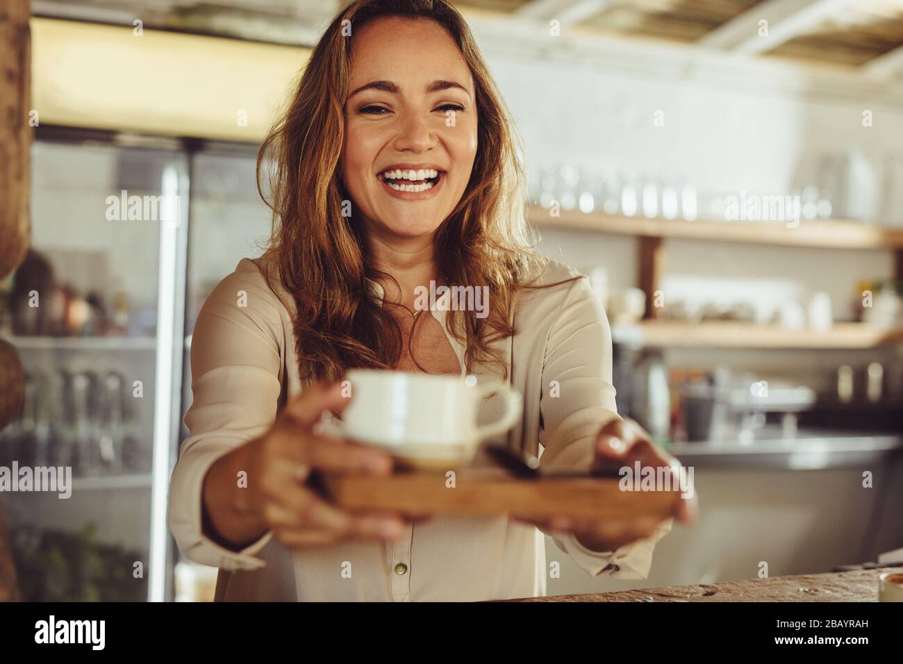 Donna sorridente che lavora dietro il bancone di una caffetteria. Buona cameriera giovane che serve il caffè al cliente in caffetteria. Foto Stock