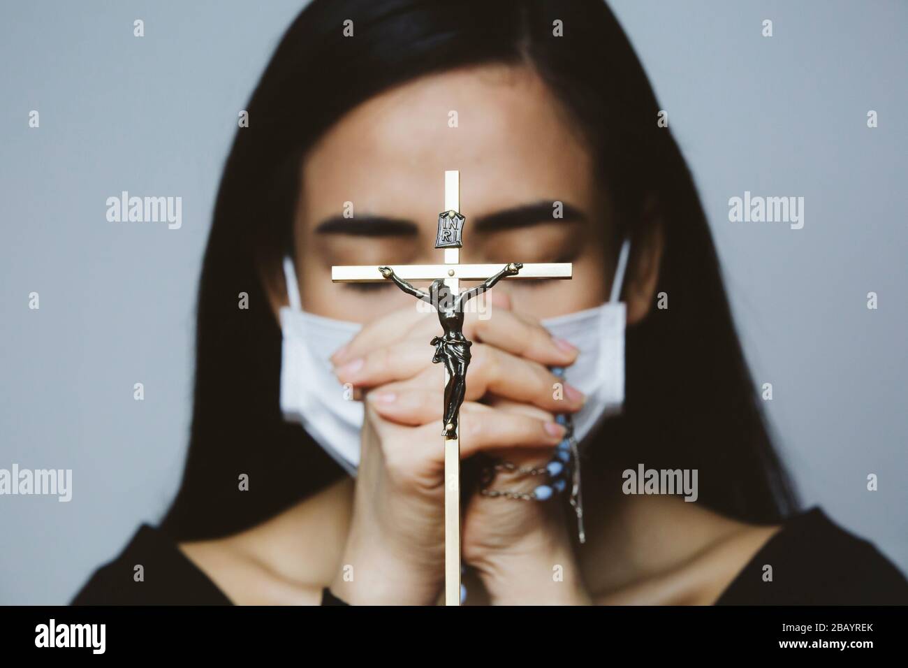 Donna che indossa maschera chirurgica che prega con rosario. Religione cristiana speranza concetto. Foto Stock