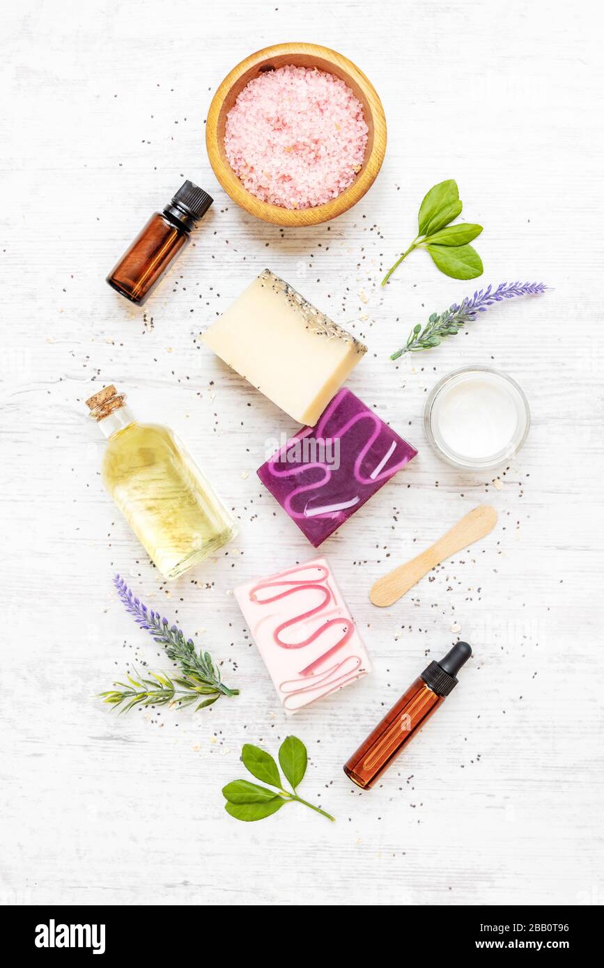 Vista dall'alto di saponi organici e cosmetici disposti con lavanda, erbe, semi di chia e oli essenziali. Sfondo rustico bianco. Foto Stock