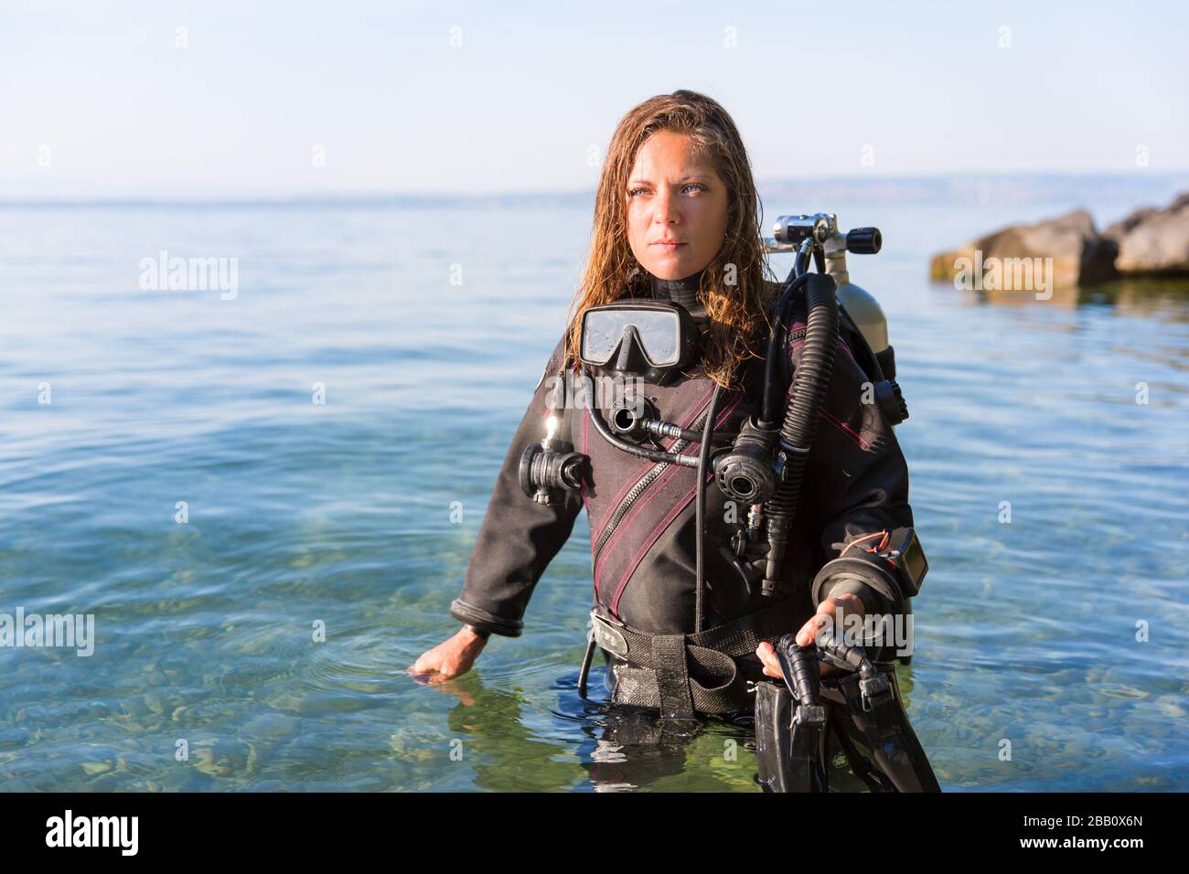 Female Scuba Diving Instructor in piedi in acqua indossando un Dry Suit, un Twin Tank e pinne di tenuta Foto Stock