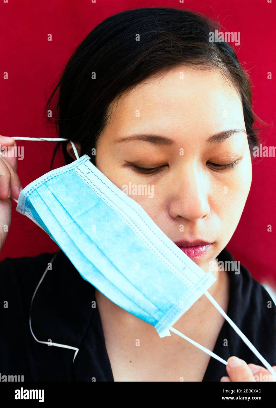 Tema del coronavirus. Donna asiatica che indossa una maschera per proteggersi da infettarsi su uno sfondo rosso. Foto Stock