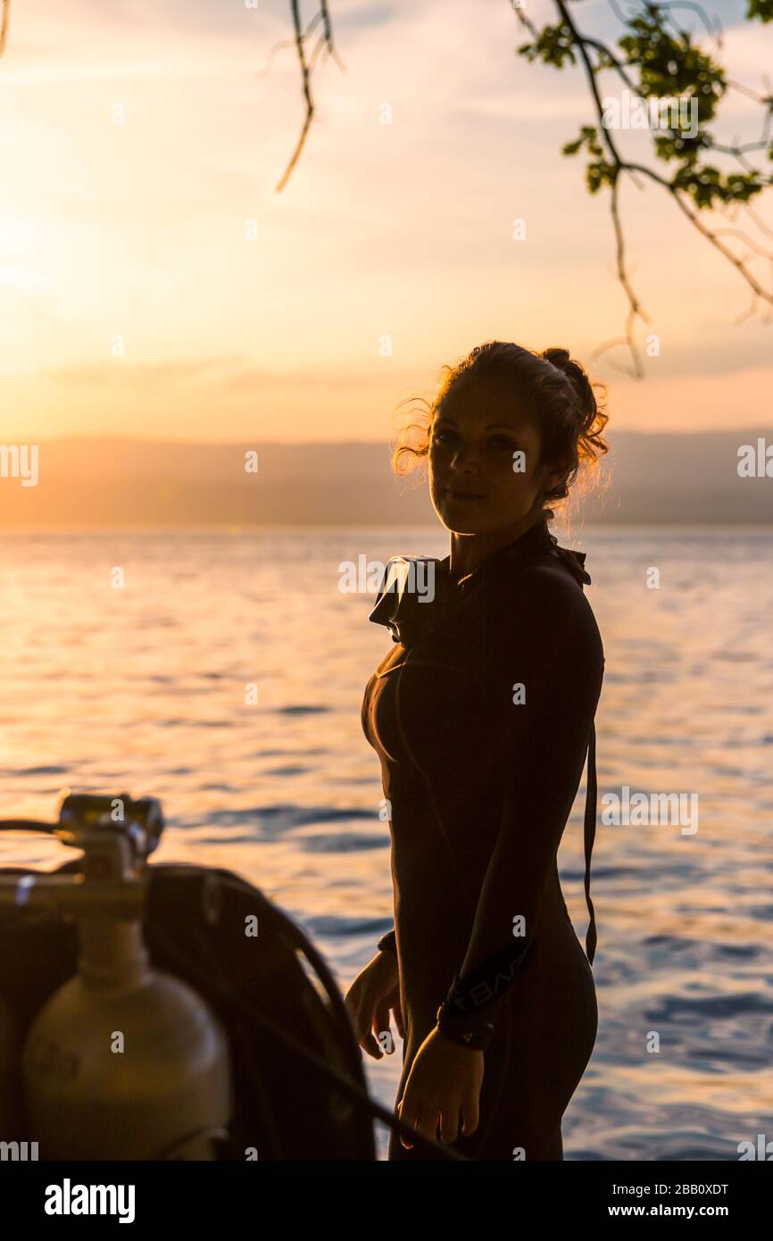 Istruttore di immersioni subacquee femminile con un costume da bagno in piedi accanto a una vasca doppia al tramonto Foto Stock
