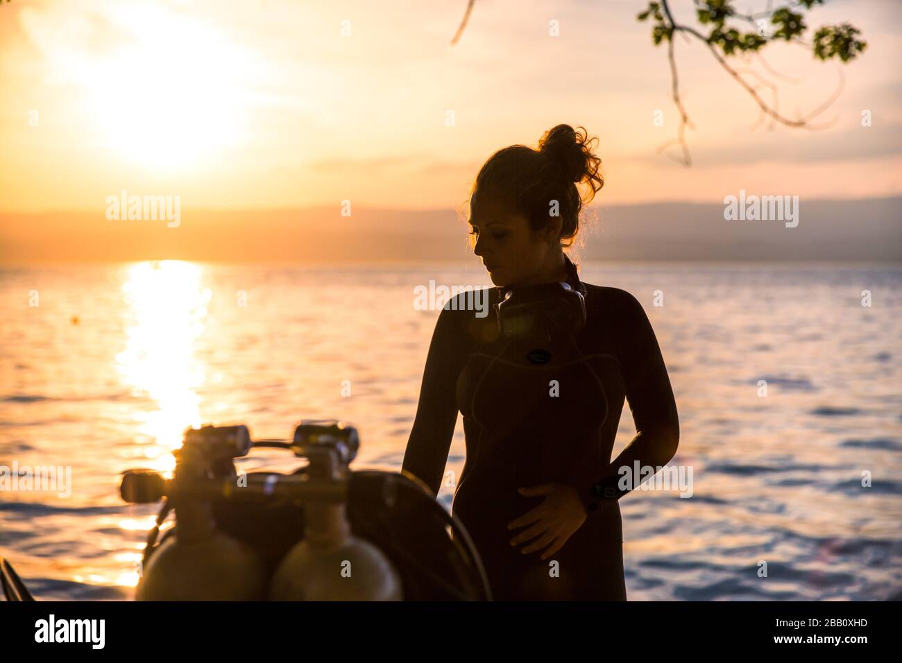 Istruttore di immersioni subacquee femminile con un costume da bagno in piedi accanto a una vasca doppia al tramonto Foto Stock