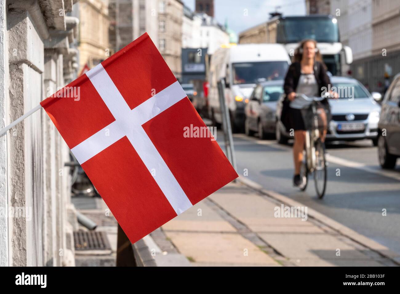 Donna che guida la sua bicicletta oltre una bandiera danese nelle strade di Copenhagen, Danimarca, Europa Foto Stock