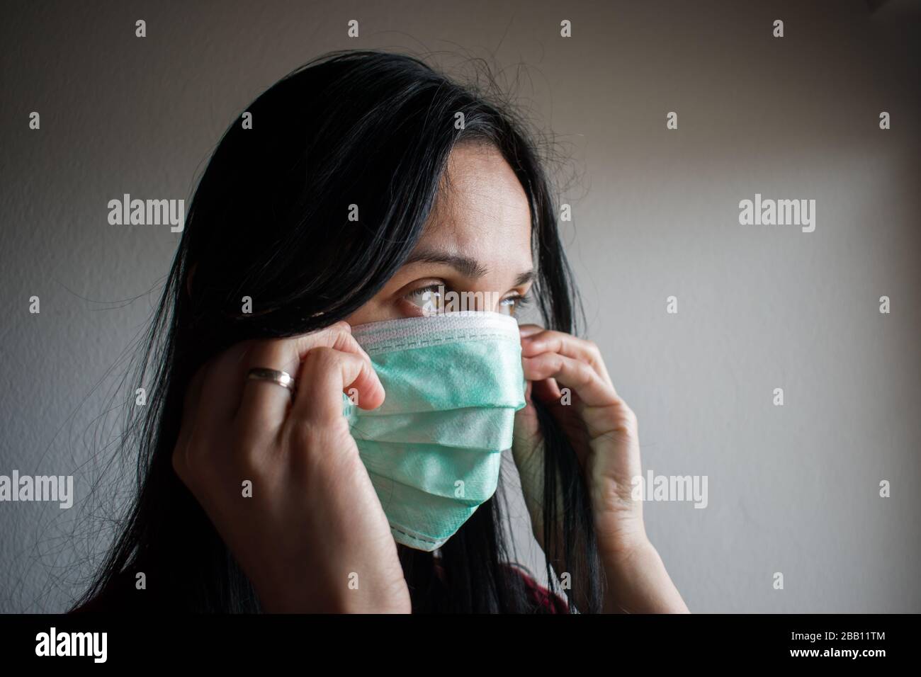 Giovane donna togliere la sua maschera medica del viso con sguardo preoccupato Foto Stock