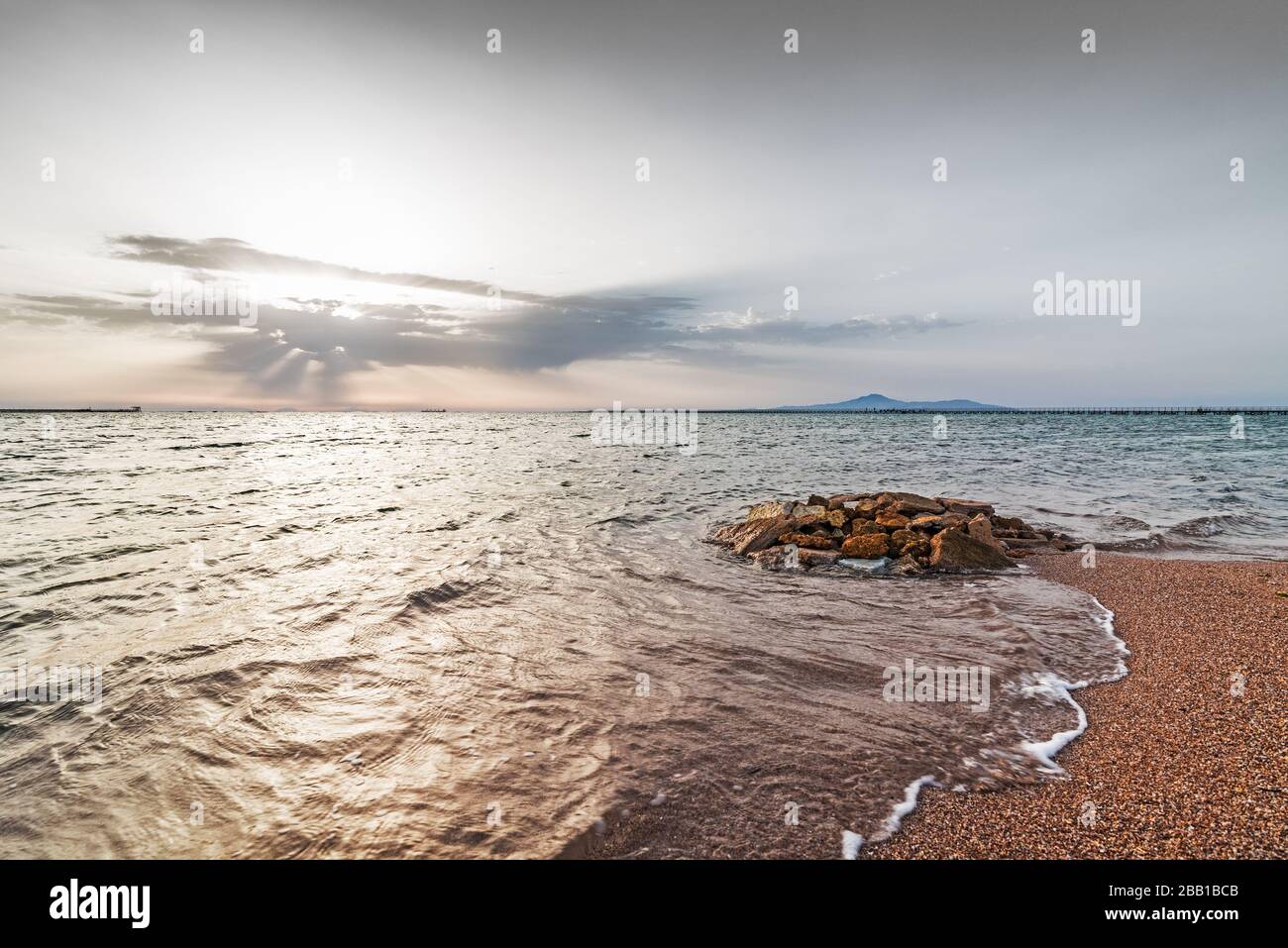 Riva del mare all'alba. L'acqua di mare si trova su pietre di diverse dimensioni e colore. Onda luminosa e rigonfiare sulla superficie dell'acqua. Mar Rosso, Sharm El Sheikh, E. Foto Stock