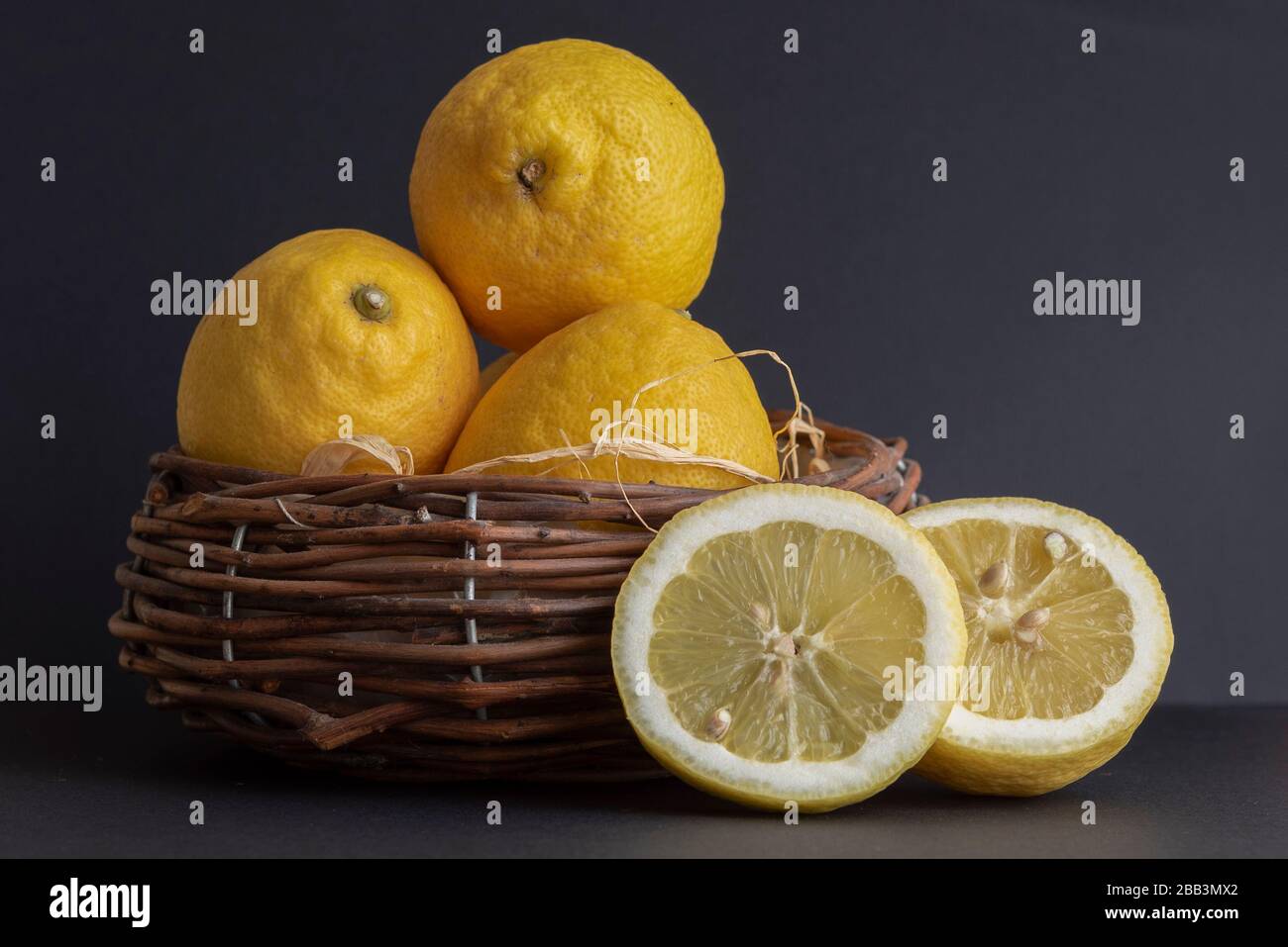 Ancora vita con limoni sorrentini freschi e fette di limone fresco in un cestino di paglia su un tavolo Foto Stock