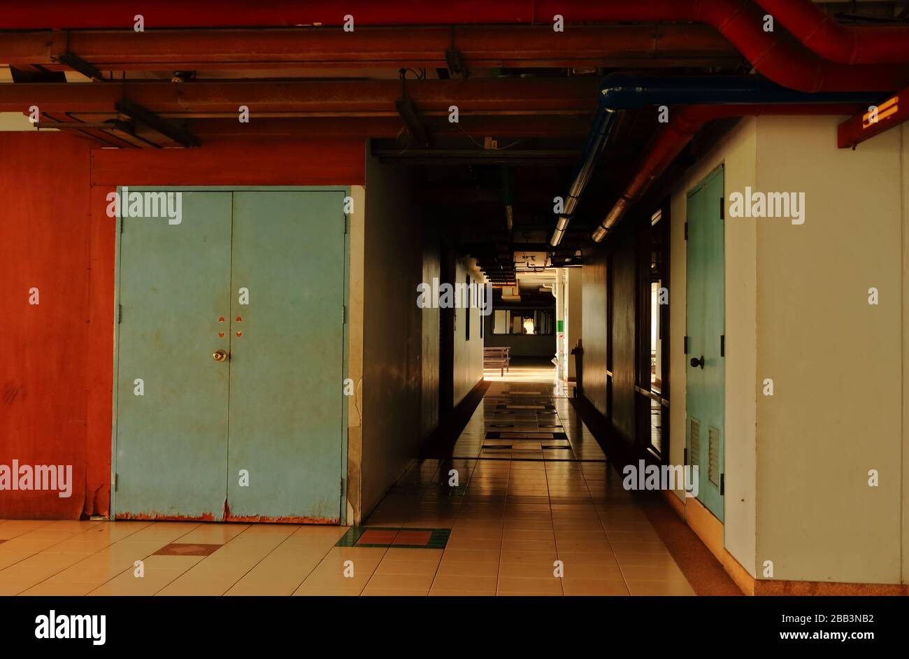 Corridoio silenzioso in un edificio vicino alla decadente porta di legno blu, con tubi d'acqua rossi installati sul soffitto Foto Stock