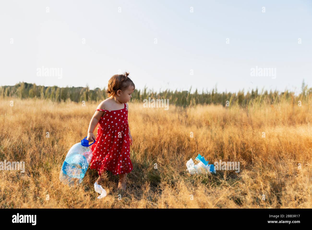 La bambina raccoglie i rifiuti sparsi nella foresta. La bambina raccoglie i rifiuti sparsi nella foresta. Il bambino lotta per un ambiente pulito. Foto Stock