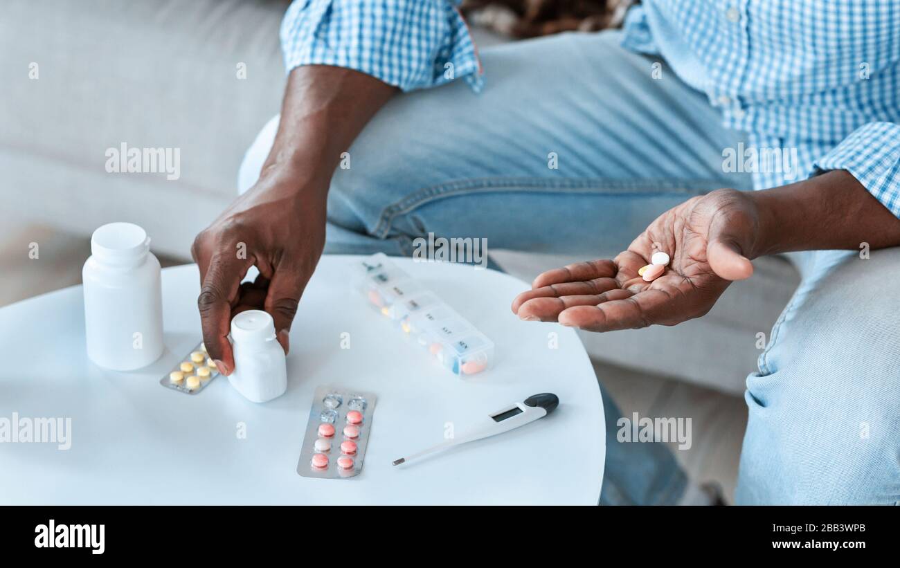 Trattamento delle malattie virali. Un uomo afroamericano irriconoscibile con diversi meds al tavolo al chiuso, primo piano Foto Stock