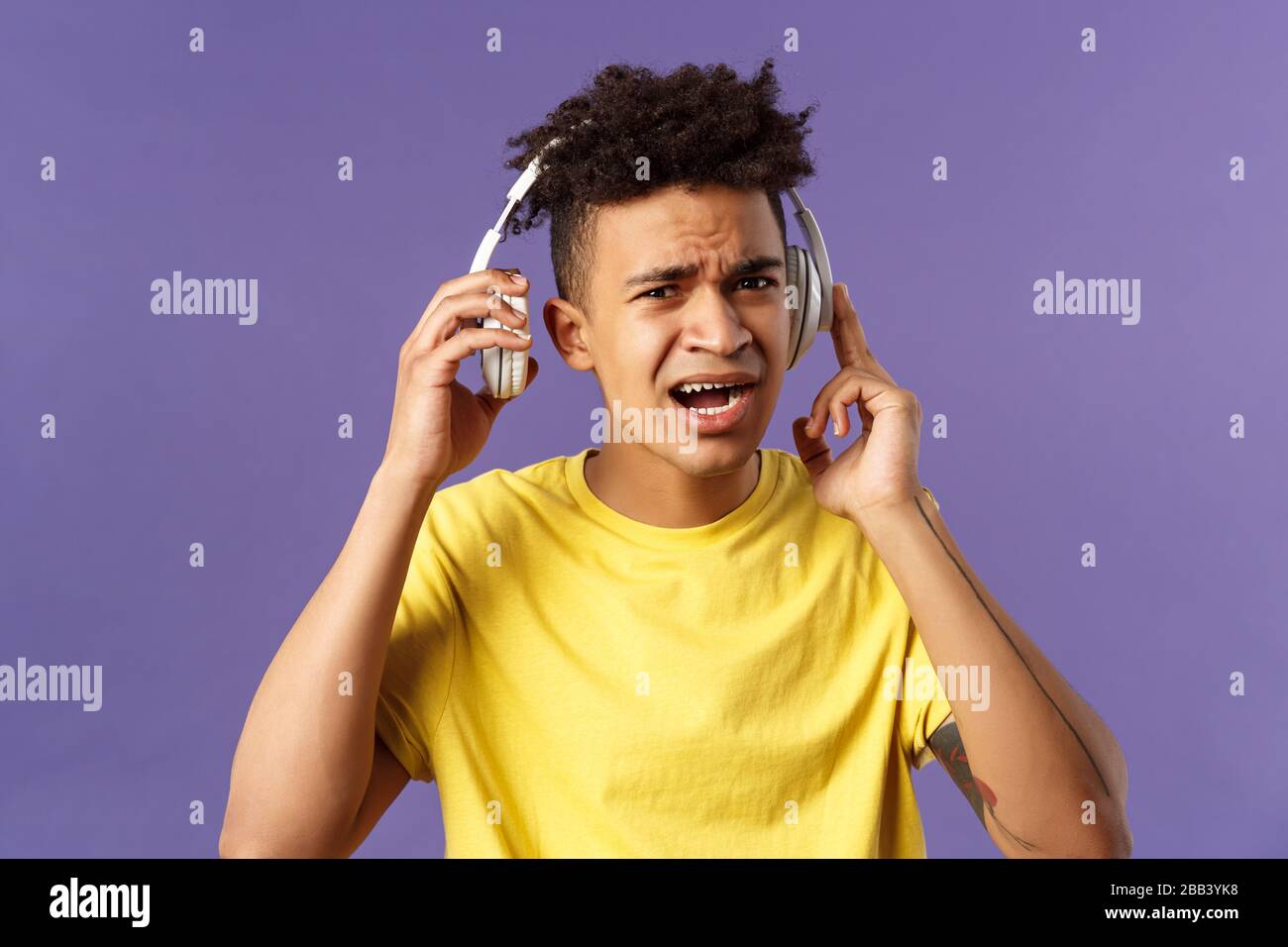 Non riesco a sentirlo, ripetete per favore. Ritratto di giovane ragazzo legato interrotto di ascoltare musica, prendere cuffie per rispondere a persona domanda, Squinting Foto Stock