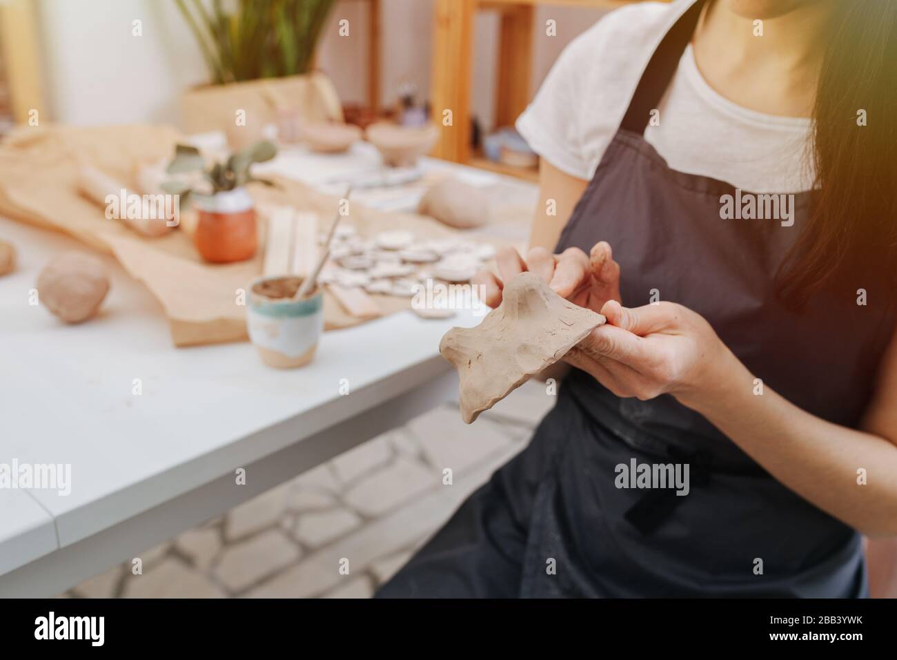 Primo piano delle mani delle donne, scolpisce dall'argilla sullo sfondo di un tavolo in uno studio di ceramica Foto Stock