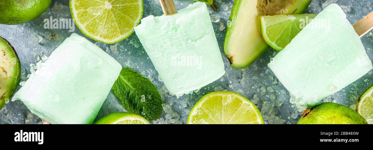 Papsicle avocado fatti in casa. Gelato vegano non caseario. Avocado, lime e cocco papsicle sano su sfondo grigio pietra con fette di calce fresca, avoca Foto Stock
