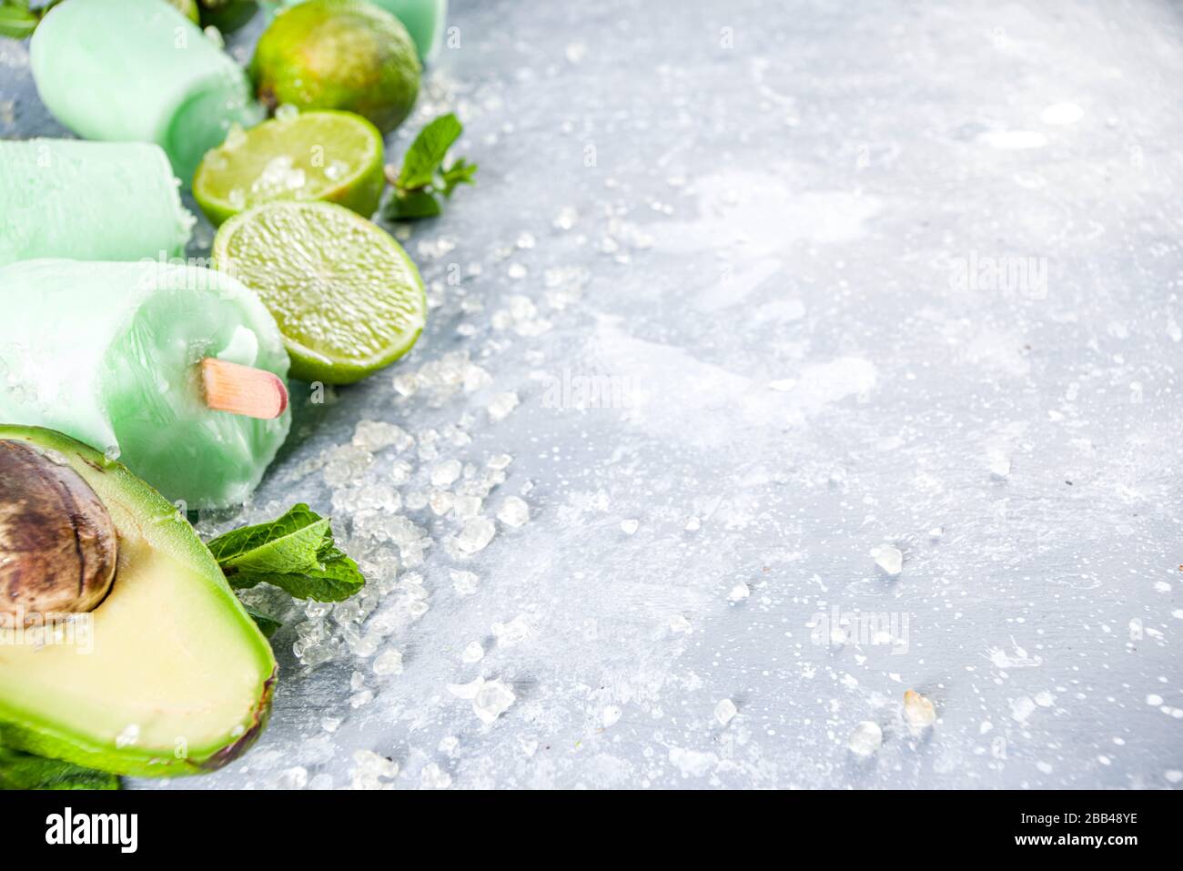 Papsicle avocado fatti in casa. Gelato vegano non caseario. Avocado, lime e cocco papsicle sano su sfondo grigio pietra con fette di calce fresca, avoca Foto Stock