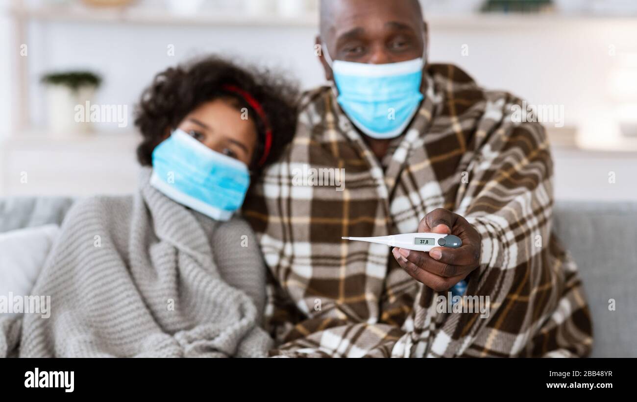 Focolaio di infezione. Famiglia americana malata che indossa maschere protettive, fuoco sul termometro nella mano del nonno Foto Stock