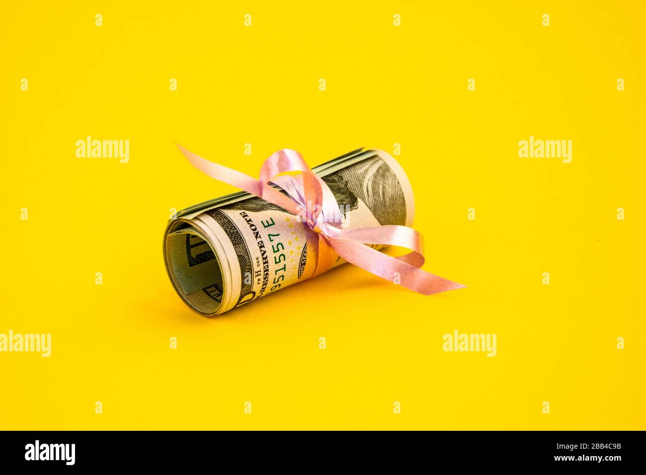 Piccolo regalo del dollaro, pacchetto delle fatture di cento dollari legati con un nastro rosa. Dollari isolati su sfondo giallo Foto Stock