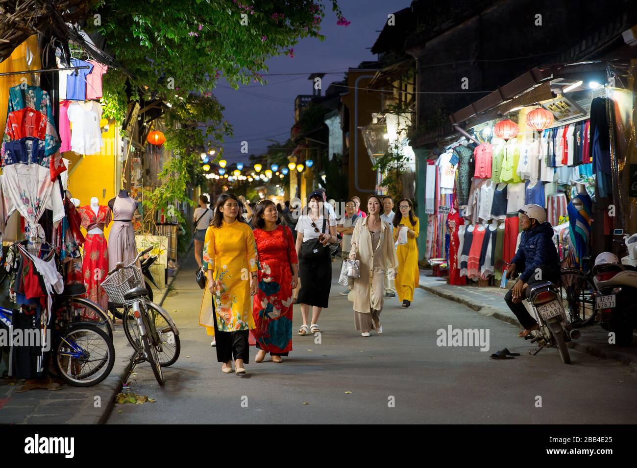 Donne in tradizionale vietnamita ao dai passeggiare attraverso il mercato notturno di Hoi An Foto Stock