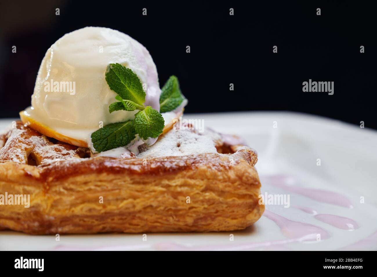Primo piano con un pezzo di torta crusty con gelato alla vaniglia bianco  sulla fetta di frutta in cima. Delizioso dessert servito con menta fresca e  zucchero a velo su piatto bianco