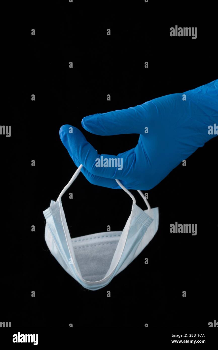 concetto di prevenzione del coronavirus . Le mani del medico nei guanti medici blu che tengono la maschera protettiva del viso isolata su fondo nero . Foto Stock