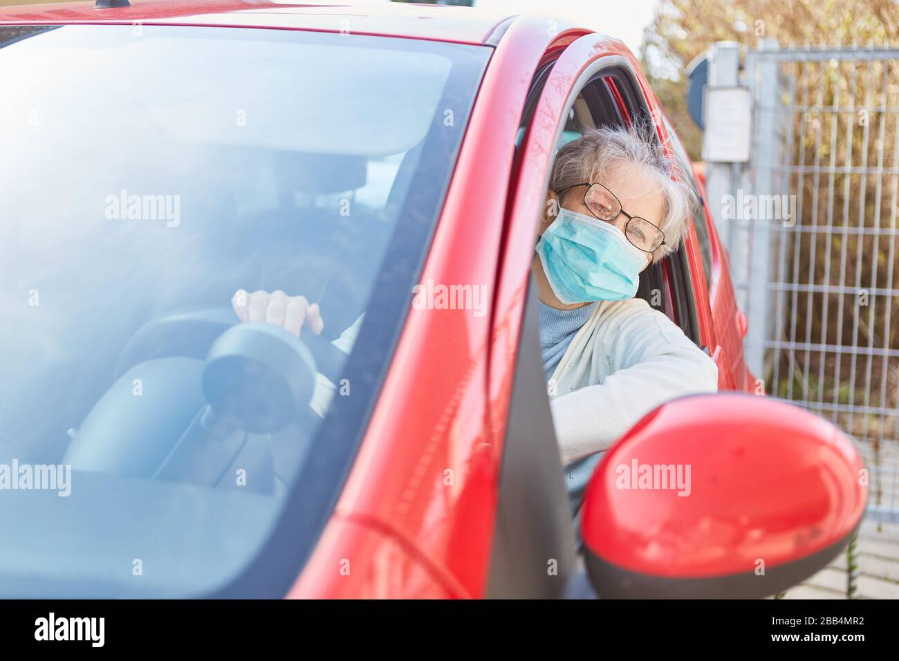 Donna anziana con maschera facciale in auto durante l'epidemia di coronavirus come protezione contro Covid-19 Foto Stock