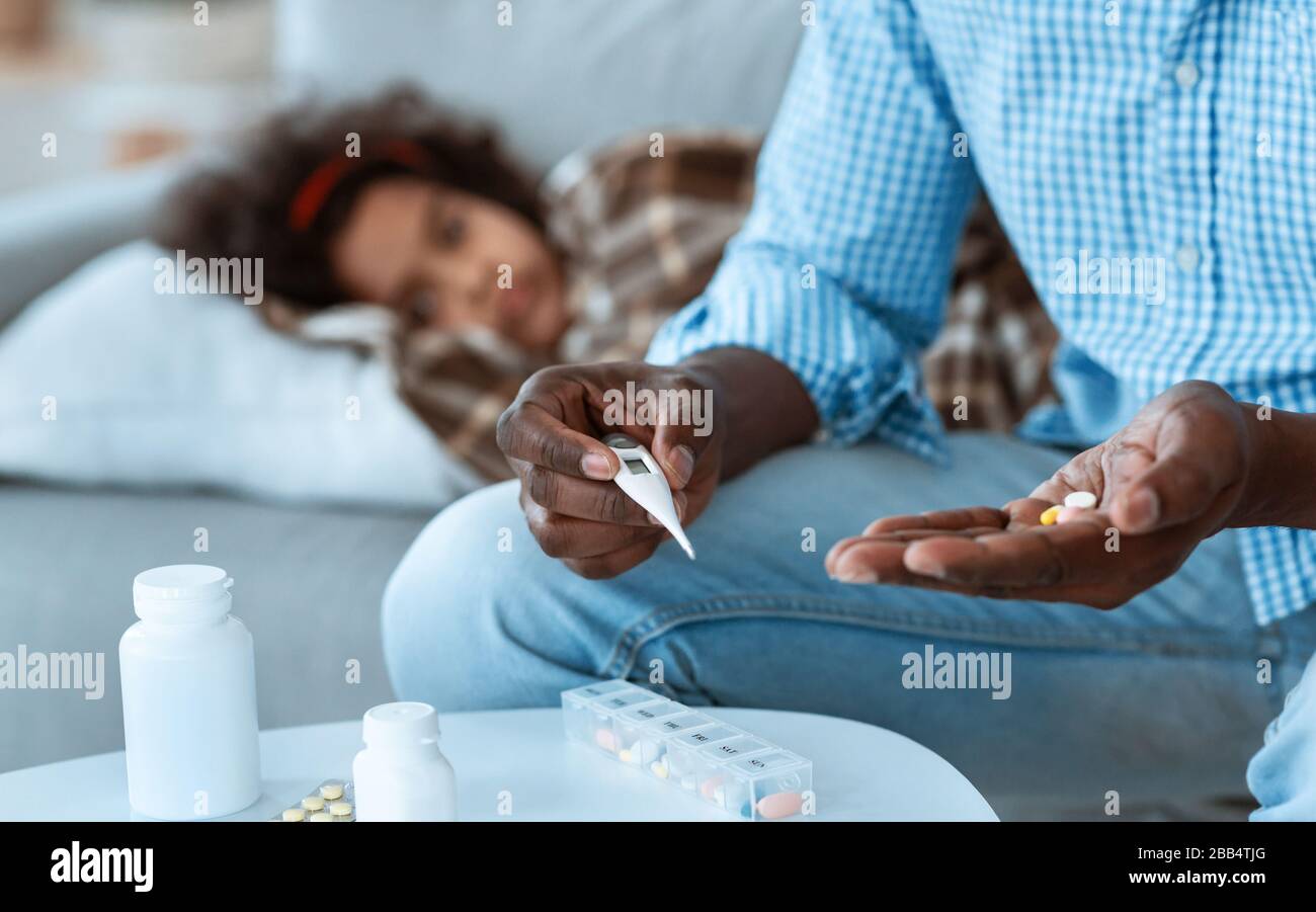 Malattia contagiosa scoppio. African American maschi tenendo pillole e termometro, bambino malato sullo sfondo. Spazio vuoto Foto Stock