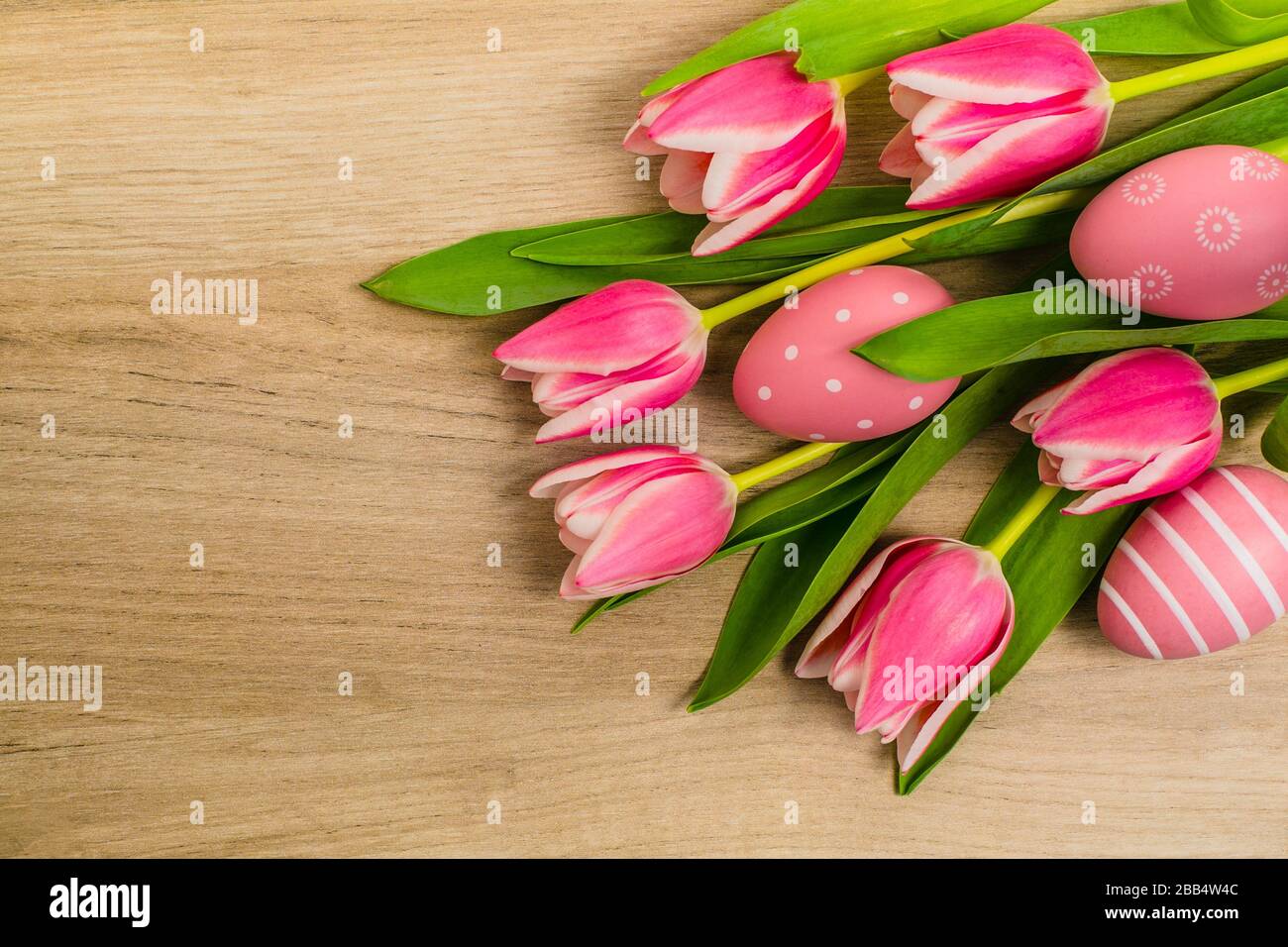 Un mazzo di fiori freschi di tulipano rosa e bianco con foglie verdi e uova di Pasqua poste su tavolo di legno, spazio copia, vista dall'alto, decorazione a pianta piatta della molla. Foto Stock