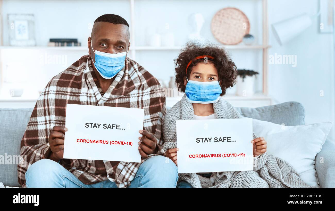 Misure di quarantena COVID-19. Ragazza afroamericana con suo nonno che rimane a casa indossando maschere protettive Foto Stock