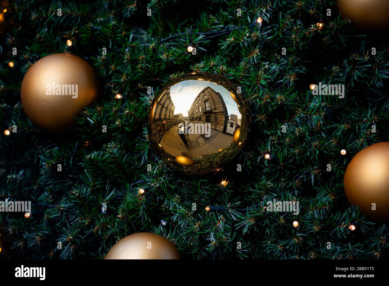 I baubles decorativi dorati appesi in un albero di Natale riflettono gli edifici esterni circostanti. Foto Stock