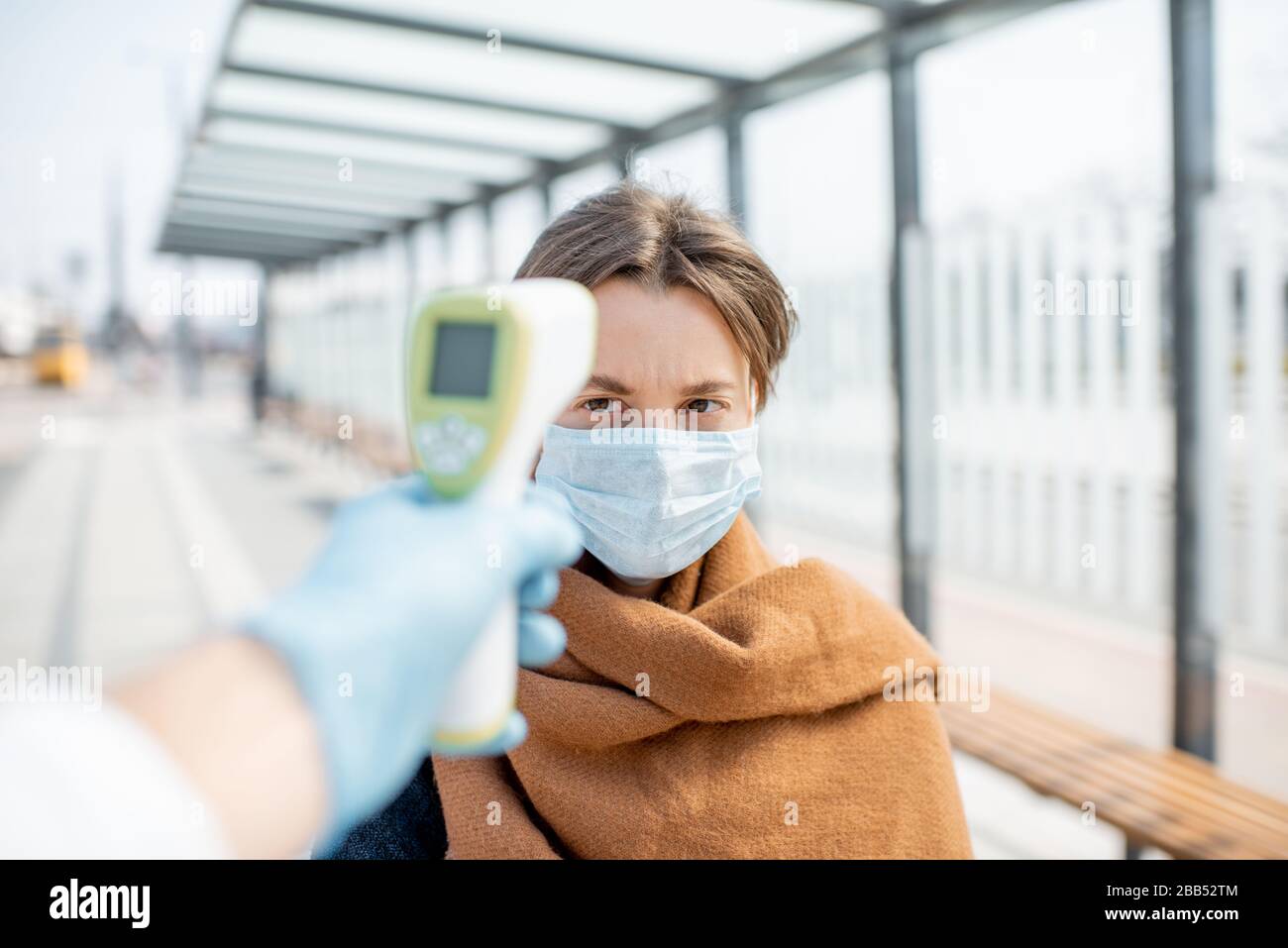 Misurazione della temperatura con termometro a infrarossi di una giovane donna in maschera facciale a un punto di controllo durante un'epidemia all'aperto. Concetto di prevenzione della diffusione del virus Foto Stock